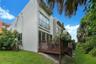 Modern two-story exterior featuring smooth stucco finish, elevated wooden deck, second-story balcony with metal railing, and extensive floor-to-ceilin