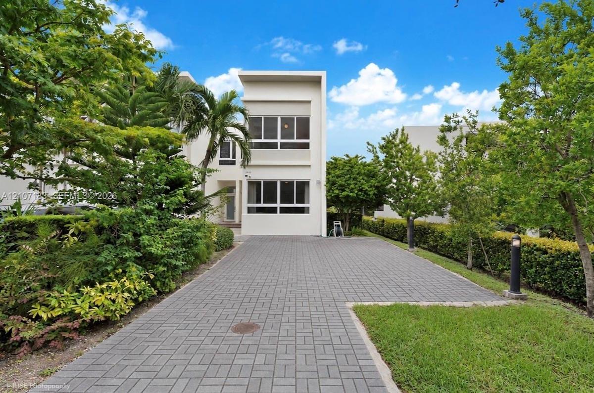 Contemporary architectural exterior with smooth white stucco facade, multi-level horizontal windows, and a paved brick driveway
