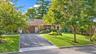 Asphalt driveway featuring a Belgian block apron, attached two-car garage, stone facade accents, and mature landscaping