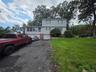 Multi-level exterior featuring light-toned horizontal siding, brick accents, a two-car garage, and expansive yard space