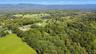 Expansive green landscape featuring abundant mature trees and distant mountain ranges under a clear sky