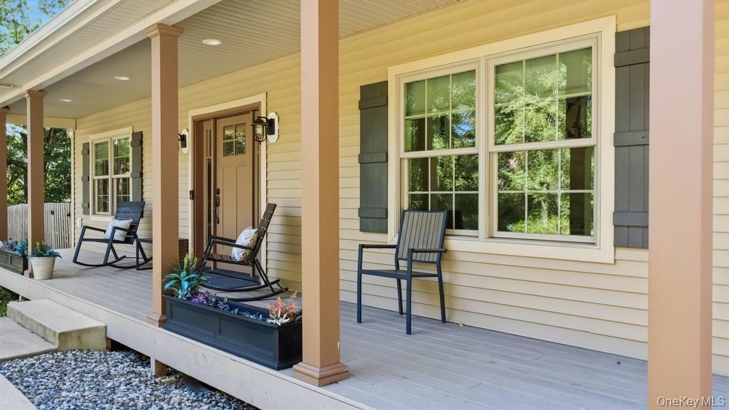 Expansive covered front porch with multiple support columns, light-toned siding, and dark shutters