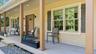 Expansive covered front porch with multiple support columns, light-toned siding, and dark shutters