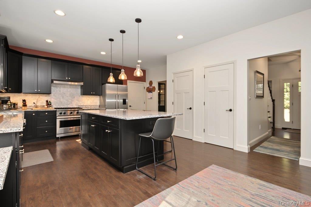 Kitchen featuring dark wood-finish flooring, black cabinetry, stone countertops, stainless steel appliances, and pendant lighting