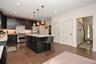 Kitchen featuring dark wood-finish flooring, black cabinetry, stone countertops, stainless steel appliances, and pendant lighting