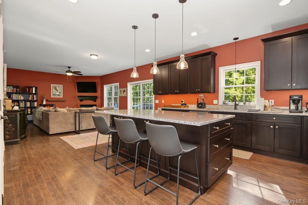 Open-concept kitchen and living area featuring wood-finish flooring, dark wood cabinetry, a center island with a light-toned countertop, and recessed 