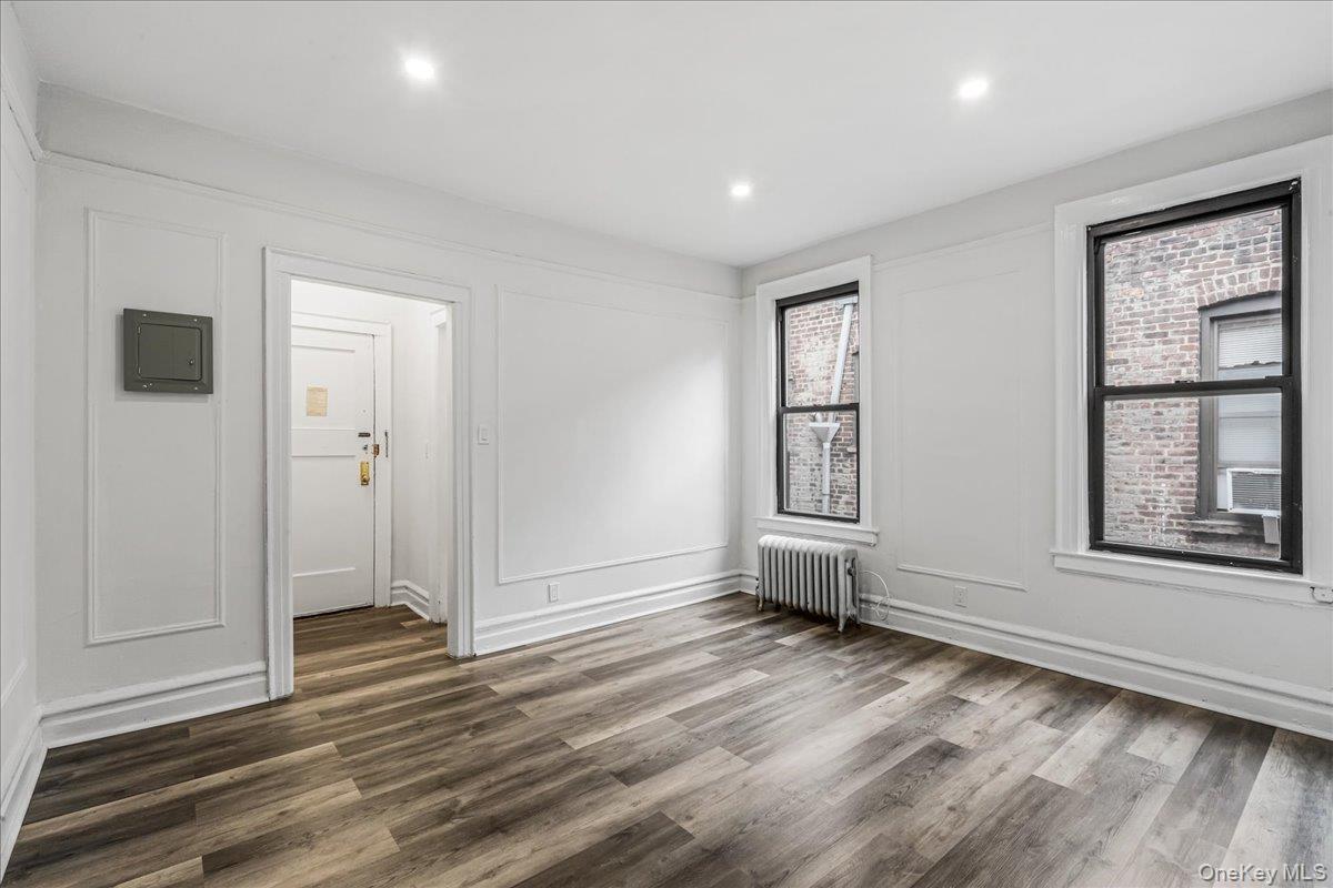Empty room with dark wood finished floors, radiator heating unit, electric panel, recessed lighting, and a decorative wall
