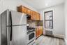 Kitchen featuring appliances with stainless steel finishes, radiator, tasteful backsplash, light wood-type flooring, and brown cabinetry