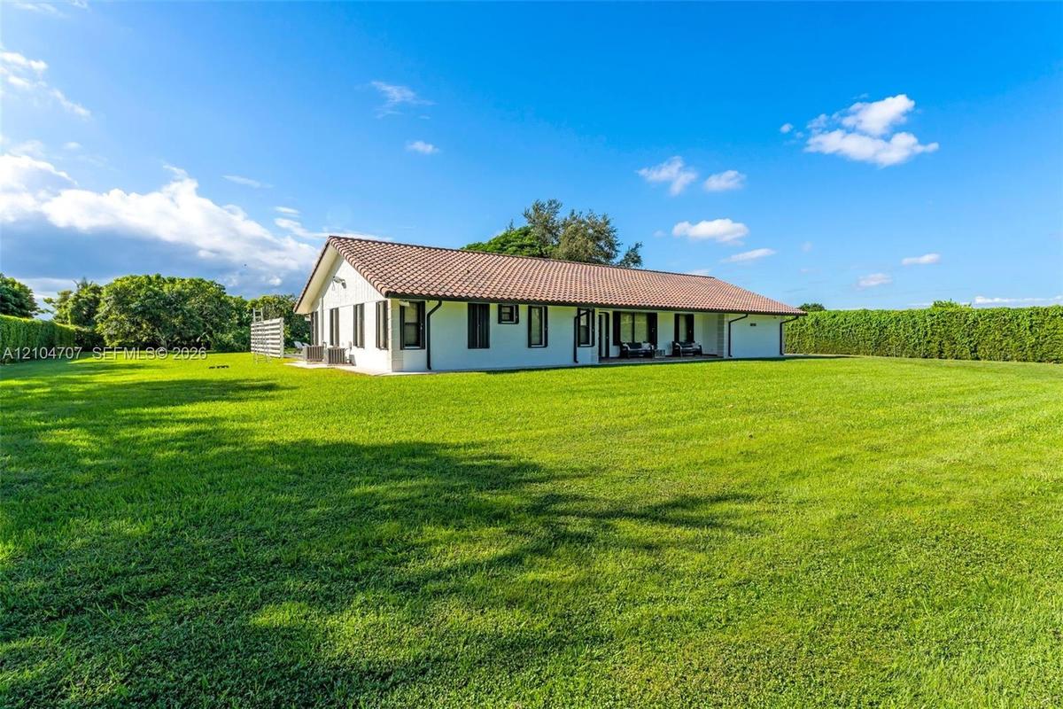 Expansive manicured lawn featuring mature perimeter hedging, a low-profile architectural structure with a tiled roof, and a covered patio area