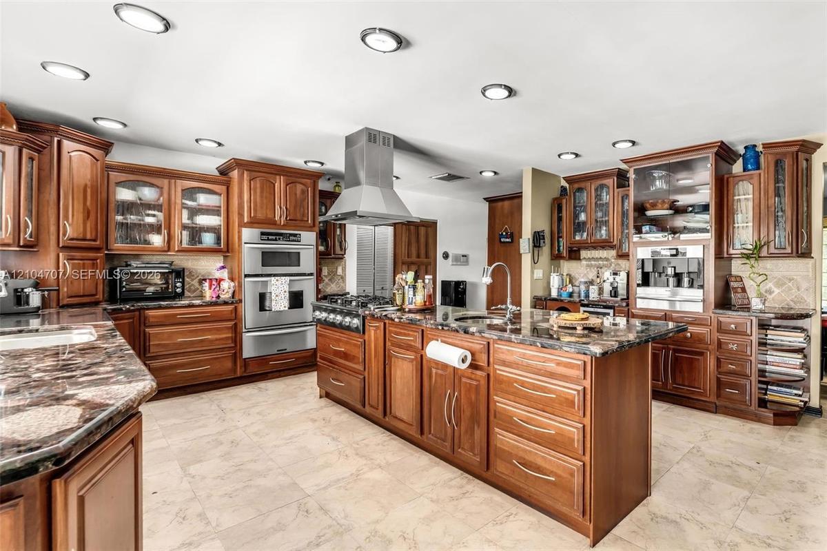 Kitchen featuring custom wood cabinetry, stainless steel gas range with a matching chimney-style hood, stone-finish tile flooring, recessed lighting, 