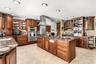 Kitchen featuring custom wood cabinetry, stainless steel gas range with a matching chimney-style hood, stone-finish tile flooring, recessed lighting, 