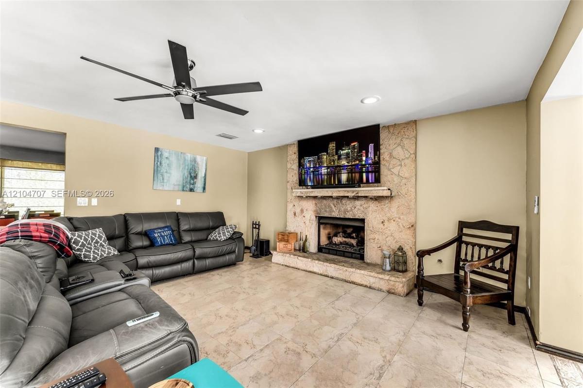 Living space featuring large-format tile flooring, a floor-to-ceiling stone fireplace surround, a raised hearth, and a multi-blade ceiling fan