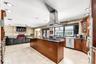 Kitchen featuring wooden cabinetry, a central island with an integrated gas cooktop, a stainless steel chimney-style range hood, stone-finish tile flo
