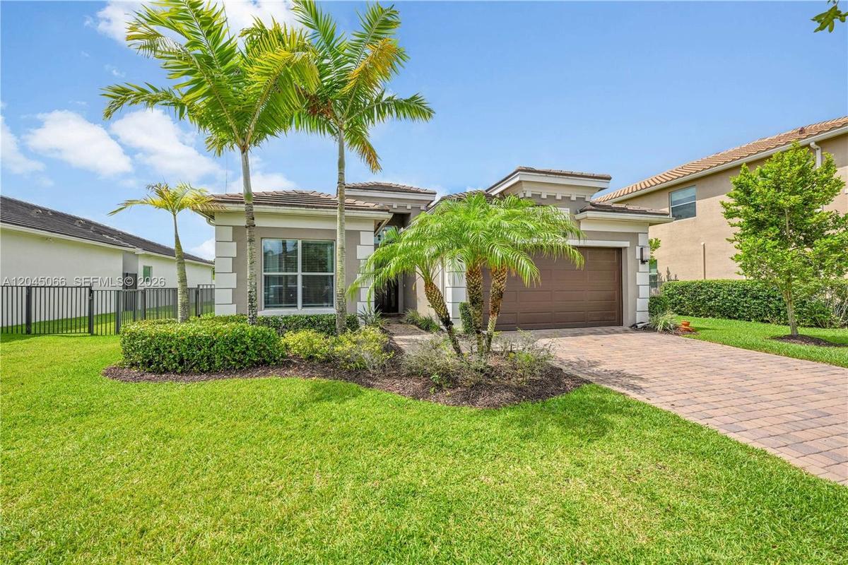 Stucco exterior with multi-level rooflines, paver driveway, single-car garage, and landscaped front yard with palm trees