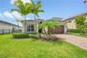 Stucco exterior with multi-level rooflines, paver driveway, single-car garage, and landscaped front yard with palm trees