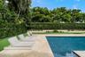 Outdoor living area featuring a custom swimming pool, travertine paver patio, synthetic turf lawn, built-in outdoor kitchen, and perimeter landscaping