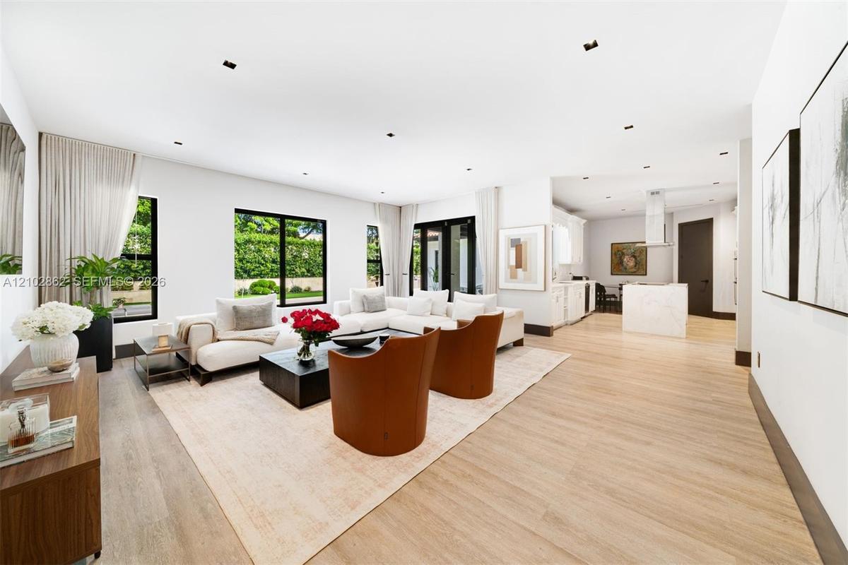 Open-concept interior featuring wood-finish flooring, recessed lighting, expansive windows with black frames, and a kitchen island with a stone-finish