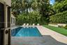 Outdoor kitchen featuring a stainless steel grill, a built-in refrigerator, stone-finish countertops, and a stone-tiled patio bordered by mature priva