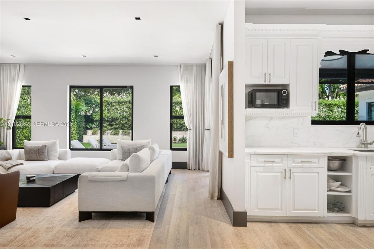 Open-concept interior featuring light wood-finish flooring, white shaker-style cabinetry, solid-surface countertops with stone-pattern veining, and mu