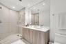 Double vanity featuring wood-finish cabinetry, solid surface countertops, dual undermount sinks, and a frameless glass-enclosed shower with tiled wall