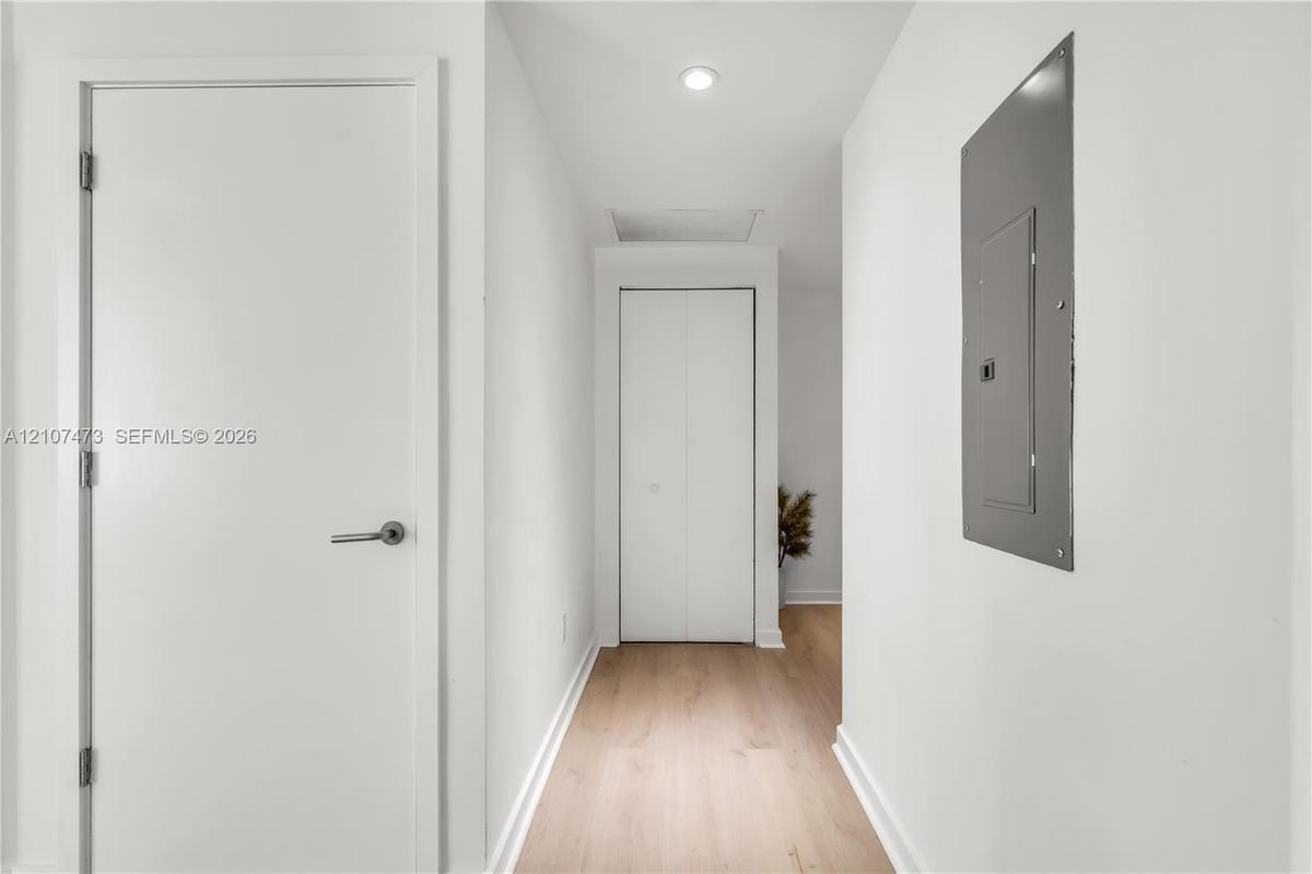 Hallway featuring light wood-finish flooring, white panel doors, recessed ceiling lighting, and a bifold closet door