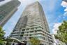 High-rise tower exterior featuring a multi-story facade, cantilevered balconies with glass railings, large-pane windows, and a structured concrete arc