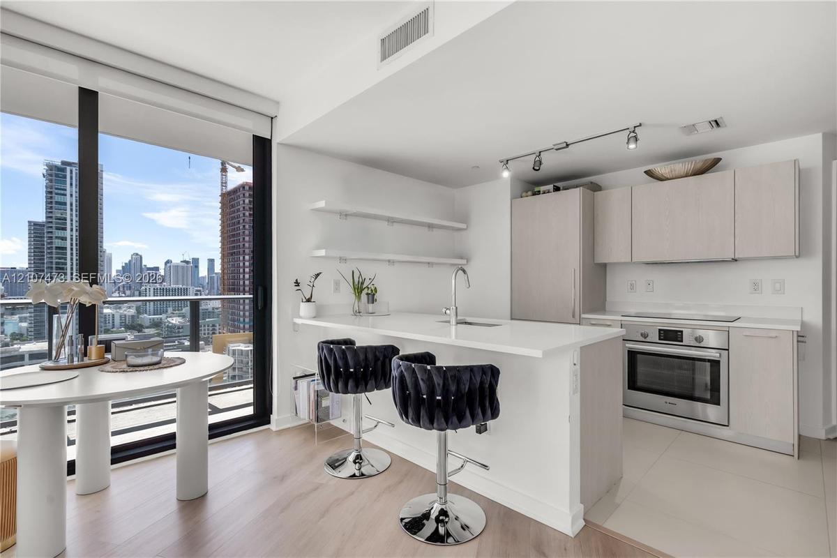 Kitchen featuring a quartz-topped island, light wood-finish cabinetry, built-in stainless steel oven, floor-to-ceiling windows, and floating shelving
