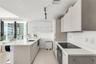 Kitchen featuring light wood-finish cabinetry, white solid-surface countertops, built-in cooktop, undermount stainless steel sink, and wall-mounted tr