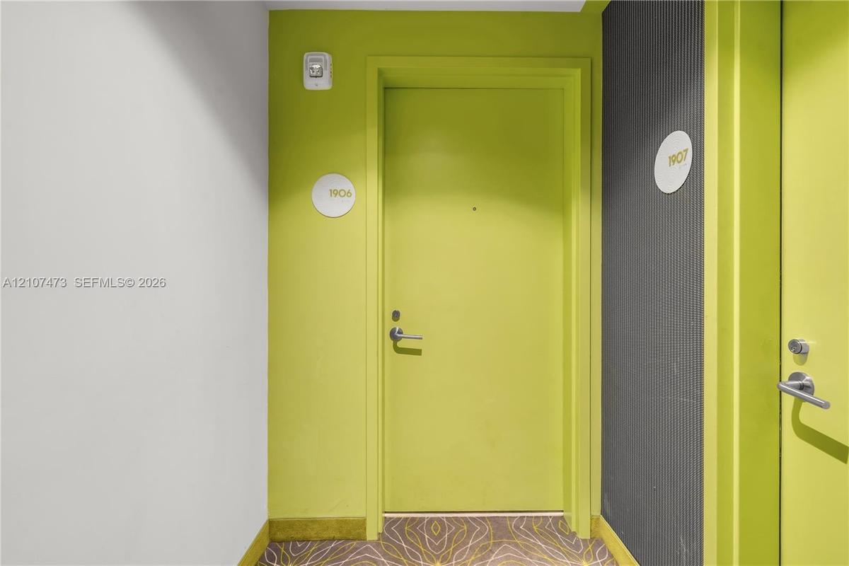 Entryway featuring lime green doors with brushed metal hardware, circular unit signage, and textured dark grey wall paneling