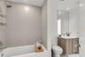 Bathroom featuring large-format wall tile, wood-finish cabinetry, a rectangular undermount sink, a tall frameless mirror, and recessed lighting