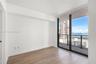Interior room featuring wood-finish flooring, floor-to-ceiling windows, and access to a private balcony with water and city skyline surroundings