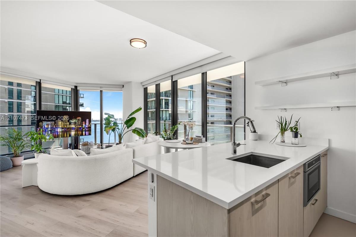 Kitchen featuring a white quartz countertop, undermount sink, gooseneck faucet, light-finish cabinetry, and built-in microwave, complemented by wood-f
