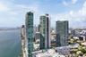 High-rise towers featuring glass facades, multi-level podium structures, swimming pools, and concrete parking facilities, situated on the waterfront