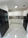 Kitchen featuring white shaker-style cabinetry, solid-surface countertops, large-format tile flooring with veined detailing, and black appliances