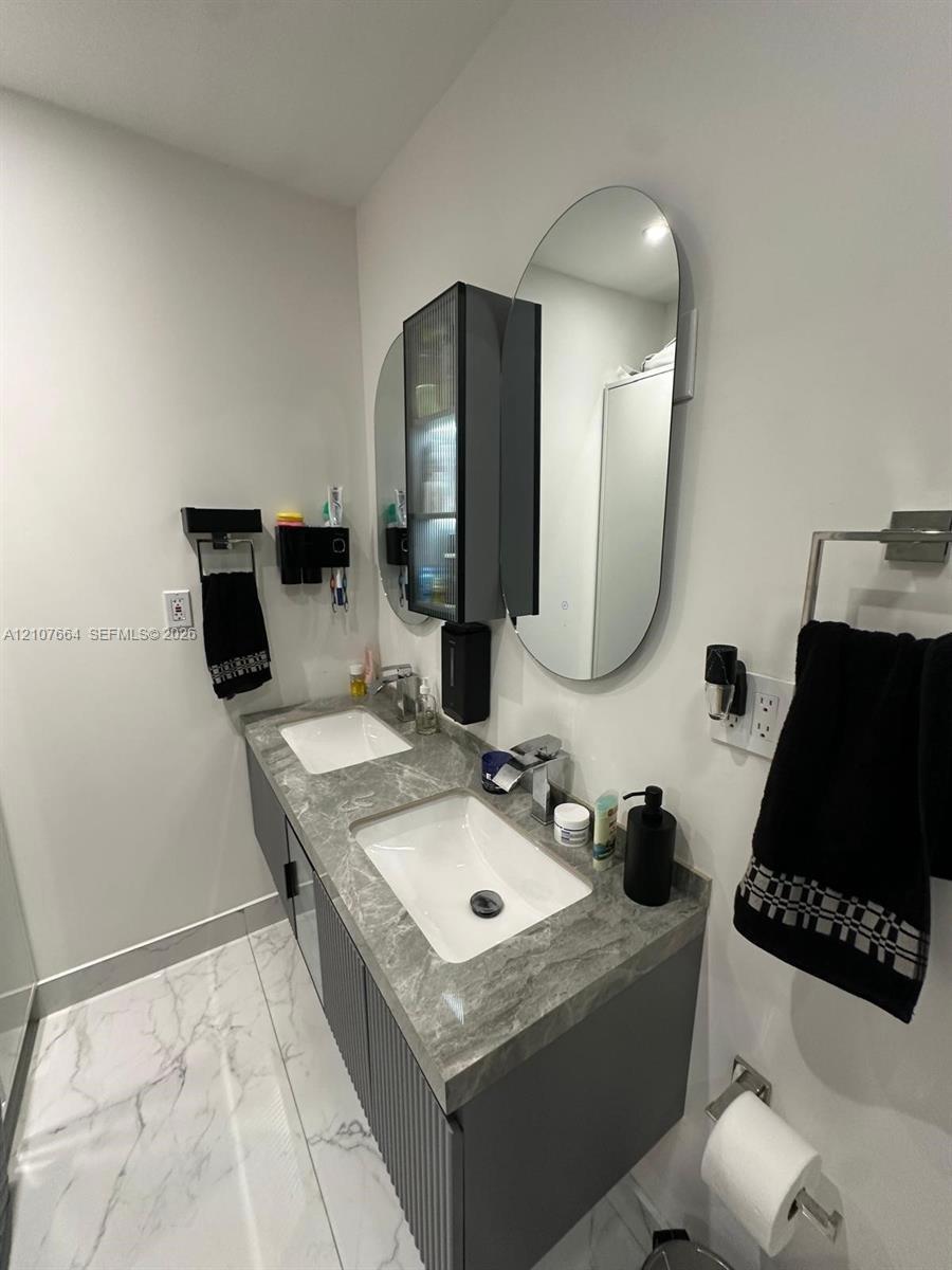 Floating double vanity featuring a grey stone-finish countertop, dual rectangular undermount sinks, vertical-slat cabinet doors, dual oval wall-mounte