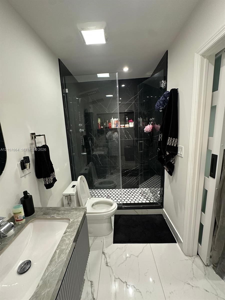 Bathroom featuring large-format white tile flooring with grey veining, a floating vanity with a stone-top integrated sink, a glass-enclosed shower wit