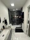 Bathroom featuring large-format white tile flooring with grey veining, a floating vanity with a stone-top integrated sink, a glass-enclosed shower wit