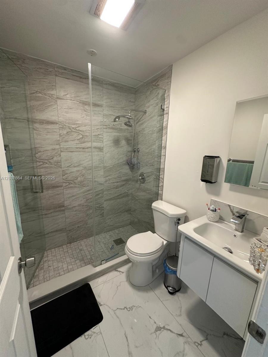 Walk-in shower with floor-to-ceiling tile, glass enclosure, and rainfall showerhead, accompanied by a wall-mounted vanity with integrated sink and lar