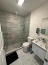 Walk-in shower with floor-to-ceiling tile, glass enclosure, and rainfall showerhead, accompanied by a wall-mounted vanity with integrated sink and lar