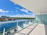 Covered balcony featuring large-format porcelain tile flooring, glass panel railings, and frosted privacy partitions, overlooking a waterfront skyline