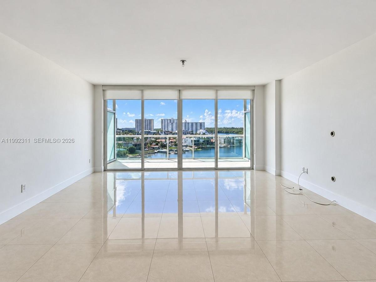 Open-concept room featuring floor-to-ceiling glass sliding doors, polished tile flooring, and a private balcony with a glass railing