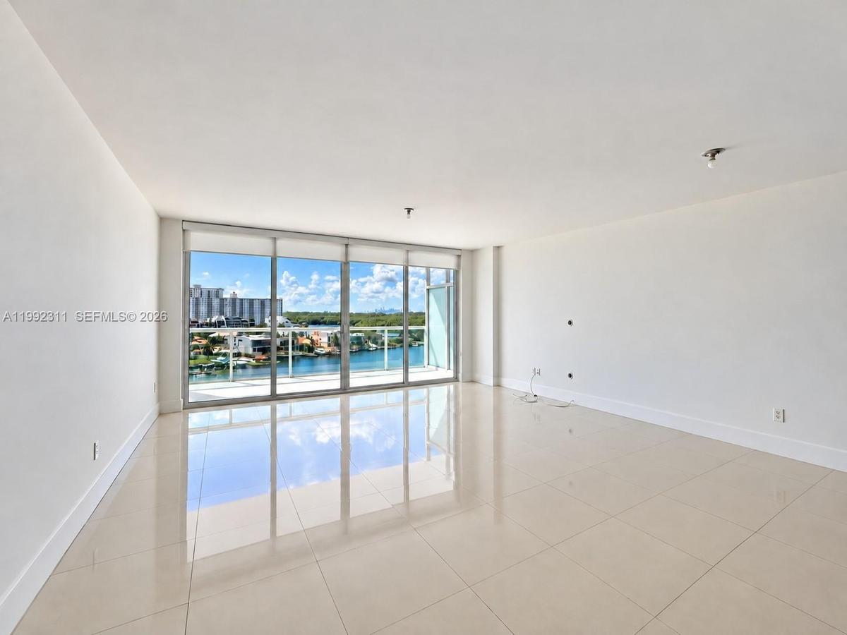 Open-concept interior featuring large-format tile flooring, floor-to-ceiling glass sliding doors, and access to a balcony with water-front scenery