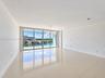 Open-concept interior featuring large-format tile flooring, floor-to-ceiling glass sliding doors, and access to a balcony with water-front scenery