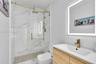 Walk-in shower with floor-to-ceiling stone-style tile, gold-finish sliding glass door, brass rain-style shower head, integrated LED-backlit mirror, an
