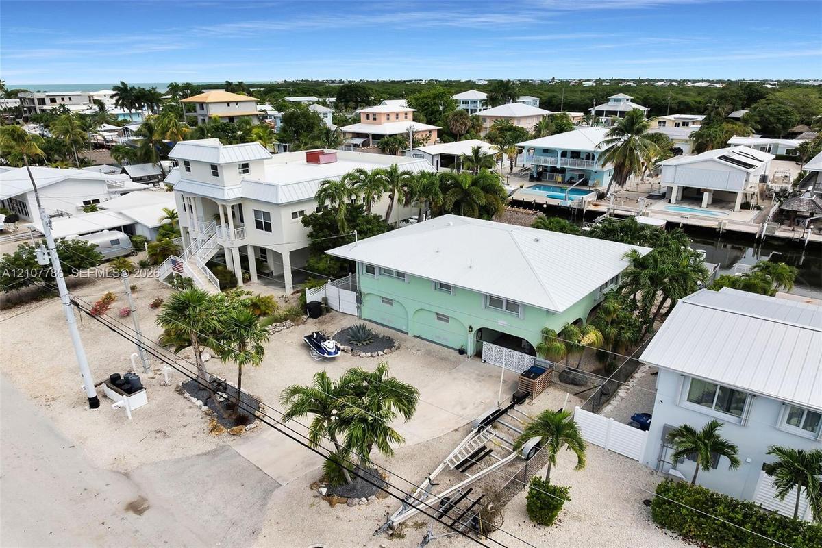 Stilted coastal residence featuring a metal roof, arched ground-level entry, concrete paved driveway, and established palm landscaping