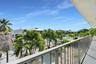 Elevated balcony featuring a metal railing and a covered ceiling, overlooking a canal-side yard with mature palm trees and natural landscaping