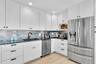 Kitchen featuring white shaker-style cabinetry, dark stone countertops, blue glass tile backsplash, stainless steel appliances, and wood-finish floori