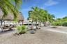 Waterfront grounds featuring a thatched-roof tiki structure, concrete walkway, gravel landscape, and palm trees