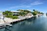 Deep-water canal frontage featuring a private dock, mechanical boat lift, concrete seawall, and mature tropical landscaping