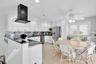 Kitchen featuring white shaker-style cabinetry, dark stone countertops, a stainless steel refrigerator, a black wall-mounted range hood, and wood-fini